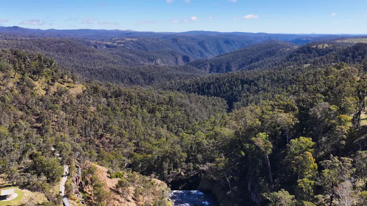 Drone footage glides above Ebor Gorge near Tamworth, revealing winding river, rugged cliffs, dense eucalyptus forest, and distant mountain ranges under bright daylight