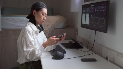 asian broker analyzing graphics on monitor and smartphone