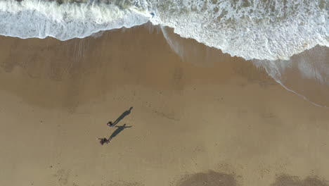 Overhead-aerial-shot-of-woman-running-towards-man-and-hugging-him-on-a-empty,-golden-beach
