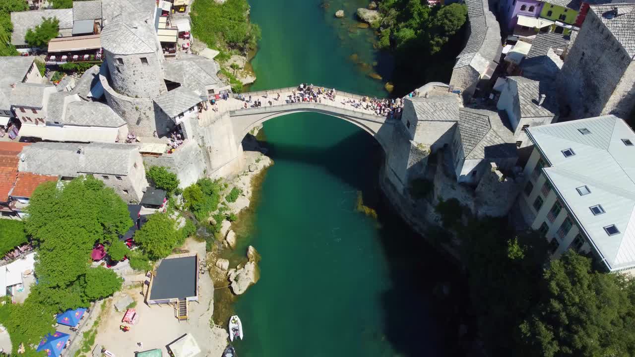 Aerial drone footage of Mostar, Bosnia and Herzegovina, showcasing the iconic Old Bridge (Stari Most), winding turquoise Neretva River, and historic Ottoman-style architecture