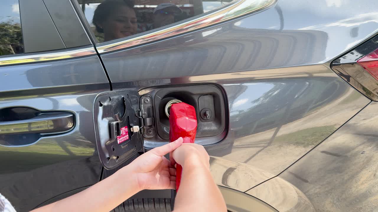 Hands remove red fuel nozzle from vehicle at outdoor gas station in bright daylight