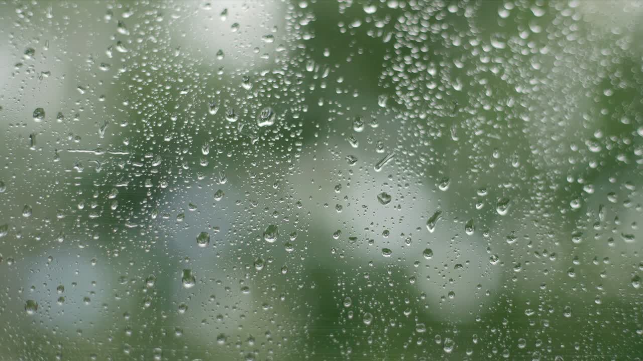 4k Close-up footage of raindrops splashing against a window glass with light leaks.