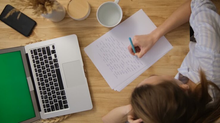 The girl writes down the main points from the conference. A laptop with a green screen. Top view. Remote work and training via the Internet. Make important notes on paper