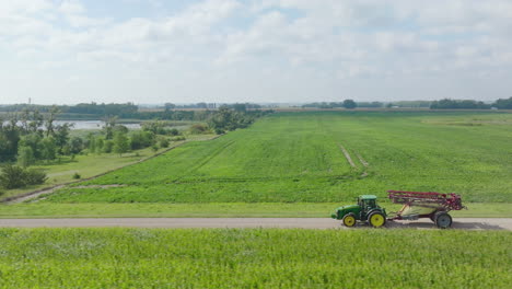 tractor with folded boom sprayer cruising along rural road adjacent to agricultural fields