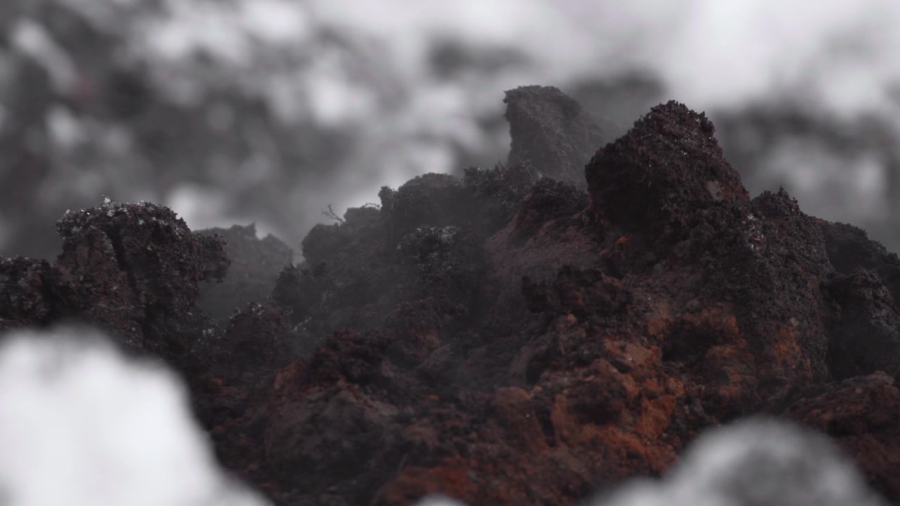 Close macro view of dark charred rock or coal like formations with rough porous surfaces, soft gray haze, blurred backdrop, and moody diffused light for dramatic industrial natural texture