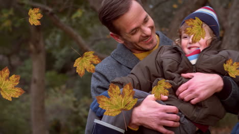 animation of fall leaves floating over happy caucasian father and son in autumn park