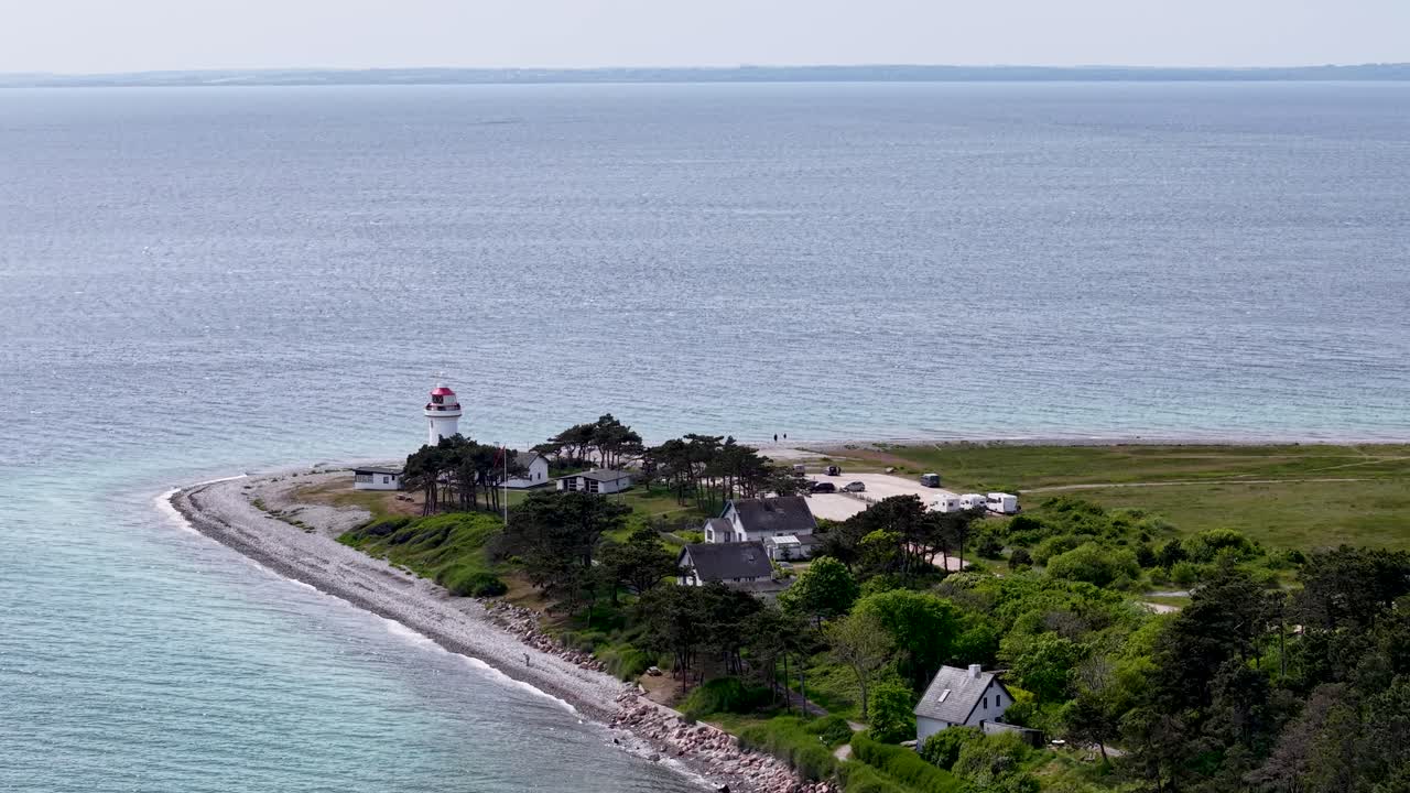 Aerial drone footage of Sletterhage Lighthouse on the Danish coast, showing the white lighthouse, rocky shoreline, and turquoise water under clear daylight