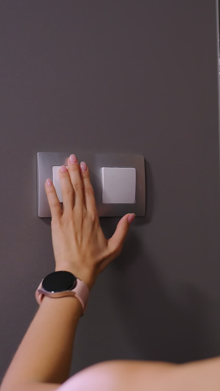 primer plano de una mujer con el cabello atado hacia atrás usando un traje marrón mientras alcanza el interruptor de luz en un interior moderno débilmente iluminado, un brillo suave destaca su silueta mientras se aleja del interruptor