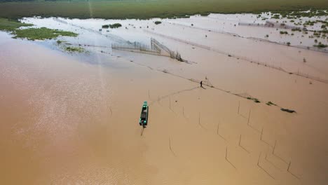 Aerial-drone-view-fly-fisherman-walking-on-water-to-attend-to-fishing-traps-on-the-Tonle-Sap,-the-largest-fresh-water-lake-in-South-East-Asia