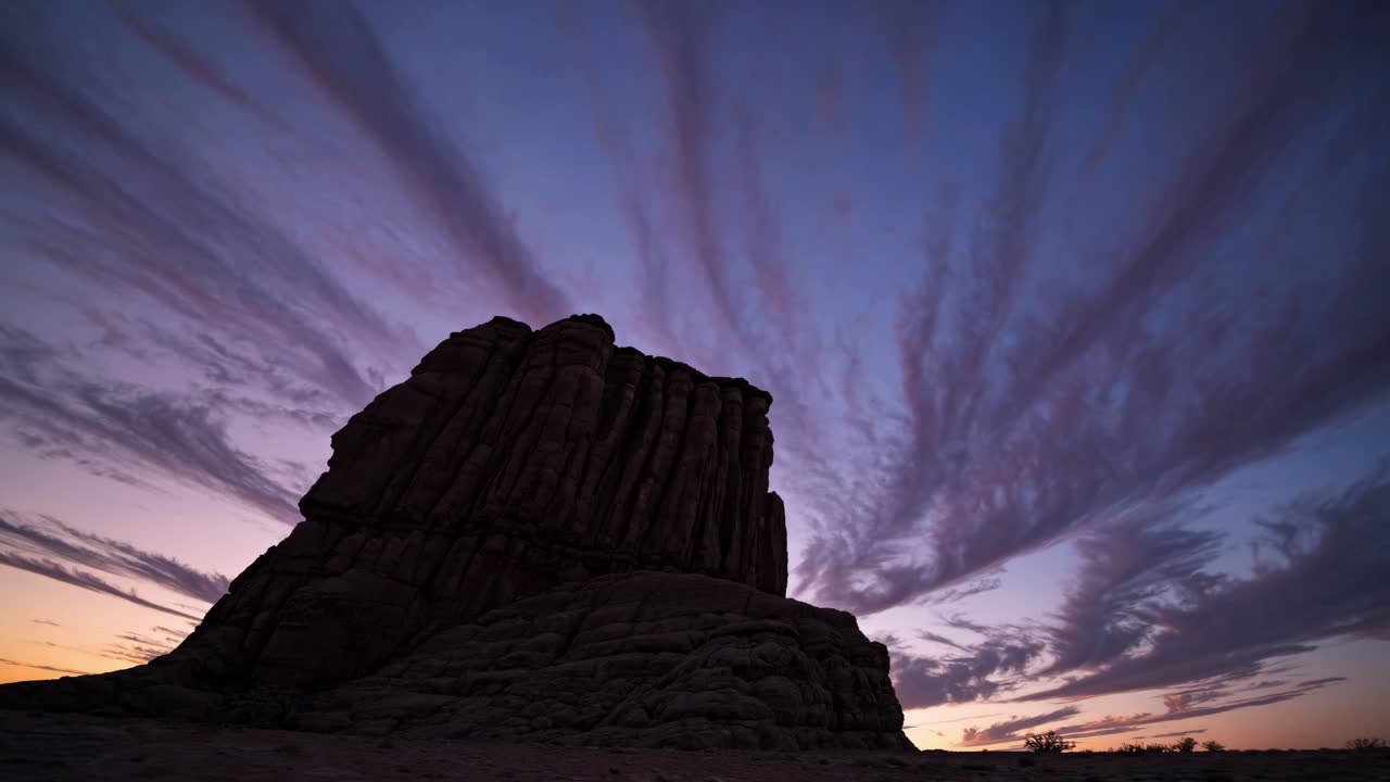Dramatic low-angle shot of a rugged rock formation at sunset, with streaked clouds radiating