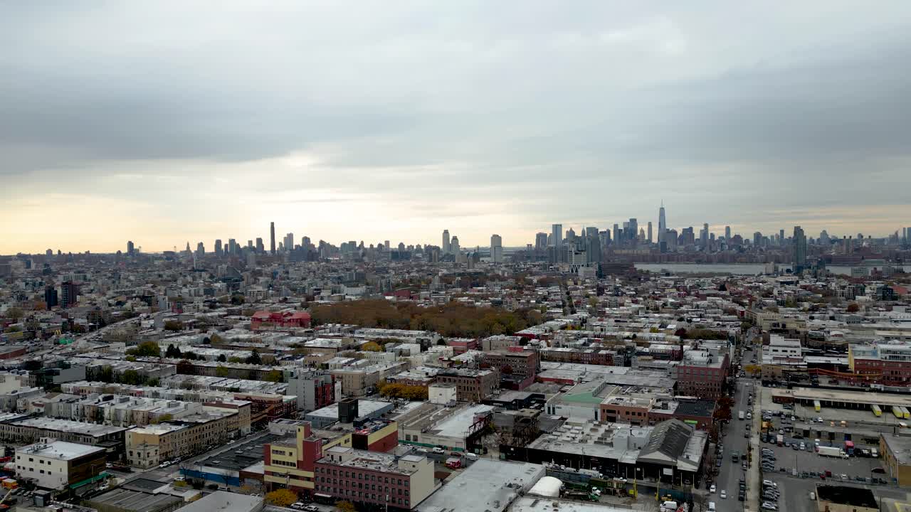 Dusk aerial flying toward Brooklyn buildings with colorful skies and lights beginning to glow across rooftops. A perfect blend of architecture, sunset ambiance, and urban energy
