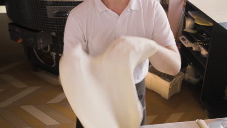 top view of a chef kneading pizza dough and waving it in the air in a restaurant kitchen