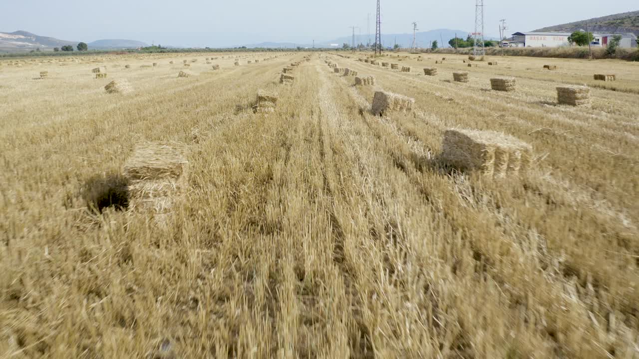 Saman balyalarıyla dolu bir römorku olan traktördeki çiftçinin havadan görünümü.
