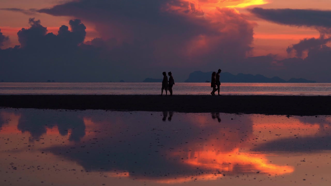 Silhouette di persone che camminano sulla spiaggia al tramonto