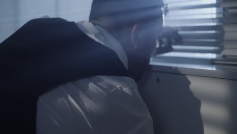 A man observes through window blinds in a suspenseful setting