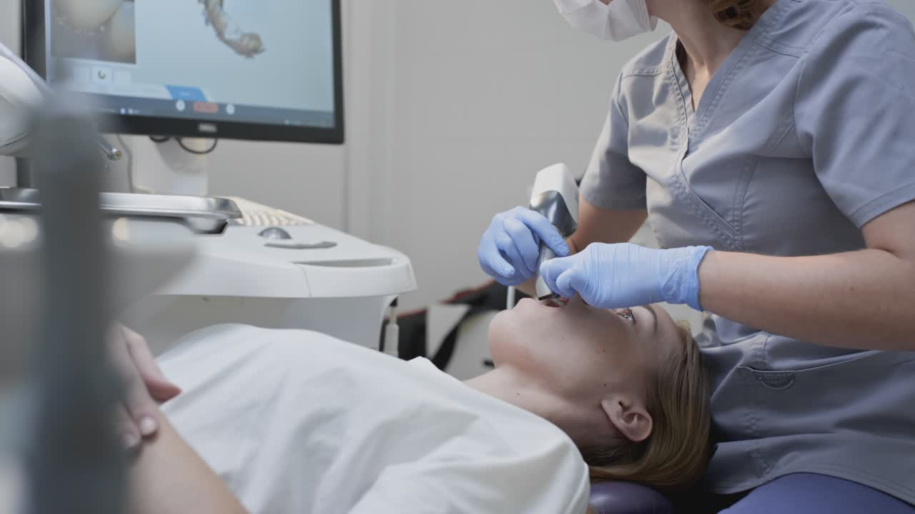Doctor scans the patient's teeth in the clinic. The dentist holds in his hand a manual 3D scanner for the jaw and mouth. Dental health. Creates a 3D model of teeth and gums on a medical monitor