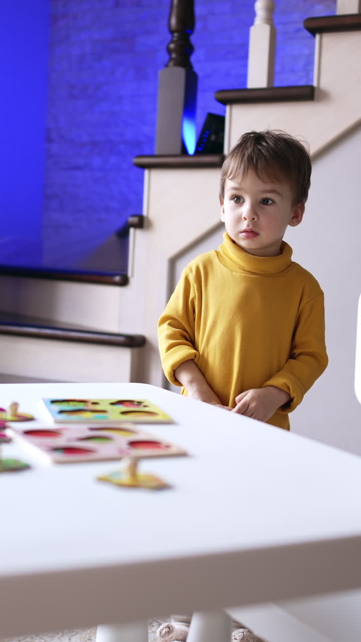 Bambino con felpa gialla in piedi vicino alla scrivania. Bambino piccolo che gira la testa verso la finestra guardando fuori. Video verticale