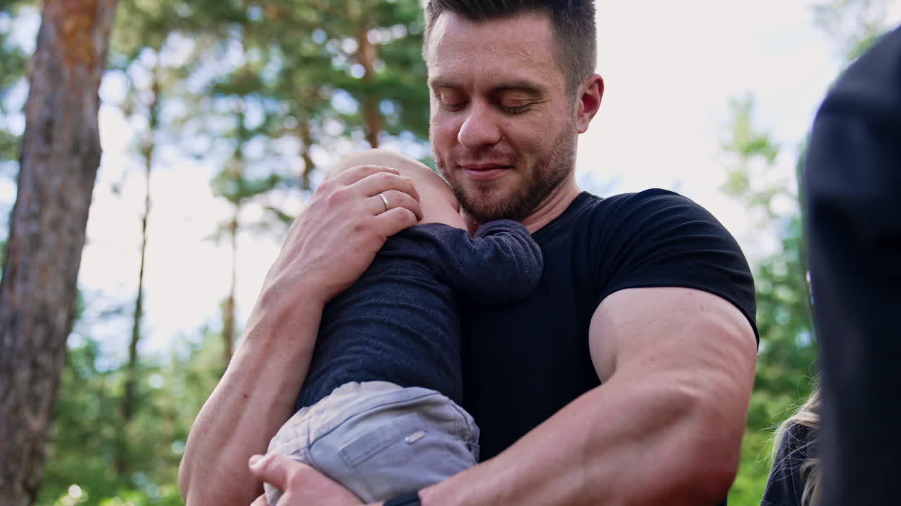Muscular Caucasian bearded man holding his newborn son. Loving dad kisses his beloved son holding him tenderly.