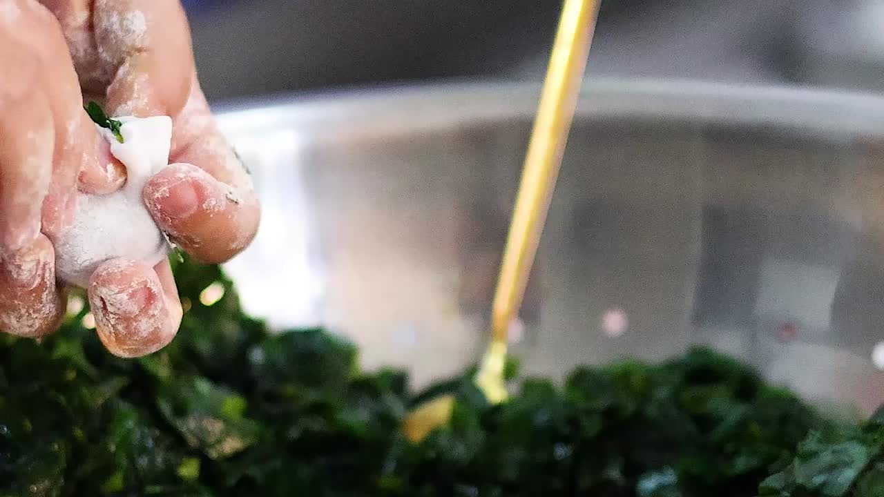 Hands and a spoon mix chopped spinach in a metal bowl, focusing on texture and movement.
