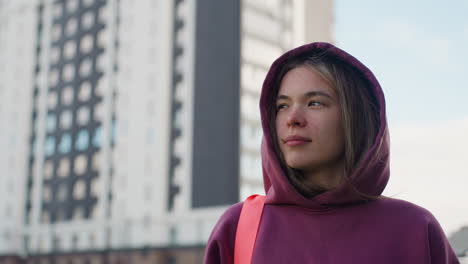 runner carrying gym bag strides along urban walkway past modern high rises with expression of relief and calm after workout, hoodie fluttering in breeze, sunlight on confident posture and serene mood