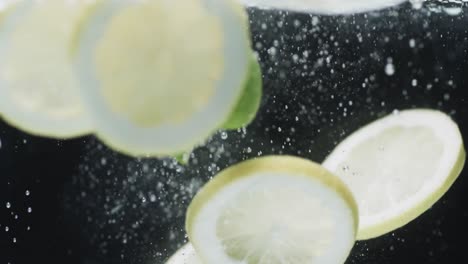 Video-of-slices-of-lime-and-lemon-falling-into-water-with-copy-space-on-black-background