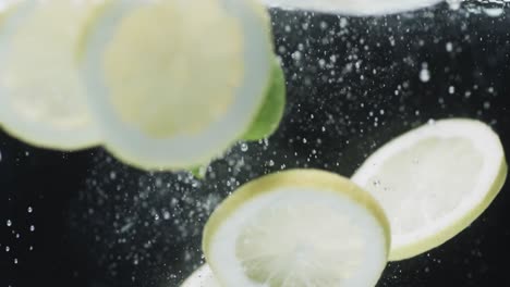 video of slices of lime and lemon falling into water with copy space on black background