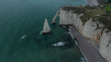 Wide-Aerial-Establisher-of-Etretat-Cliffs-Arch-on-Overcast-Day-with-dark-blue-ocean