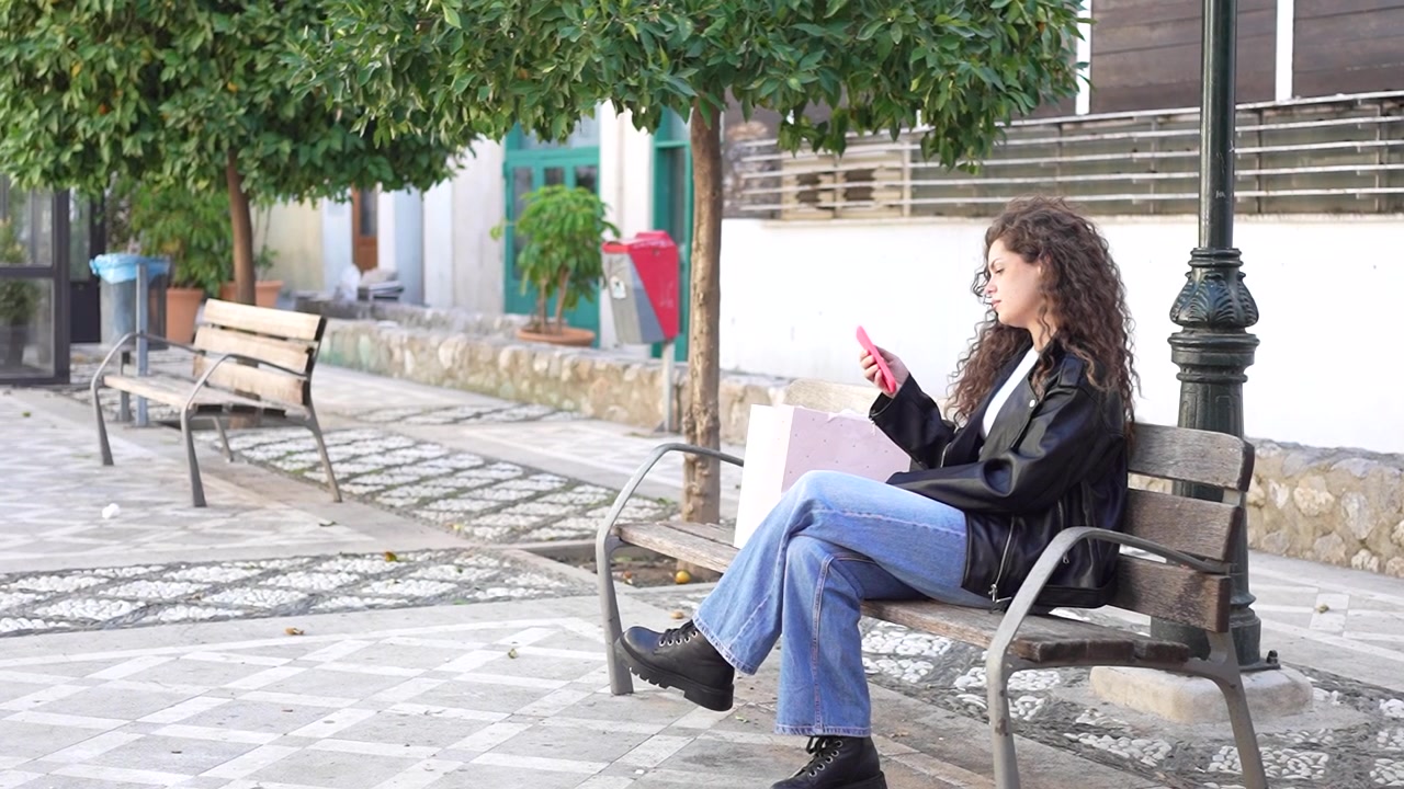 Una giovane donna è seduta su una panchina del parco, godendosi il suo tempo libero mentre usa uno smartphone.