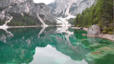 Drone-Delantero-Disparó-Alrededor-De-Un-Modelo-Masculino-De-Pie-Sobre-Una-Roca-Con-Vistas-Al-Lago-Braies-En-Los-Dolomitas,-Italia