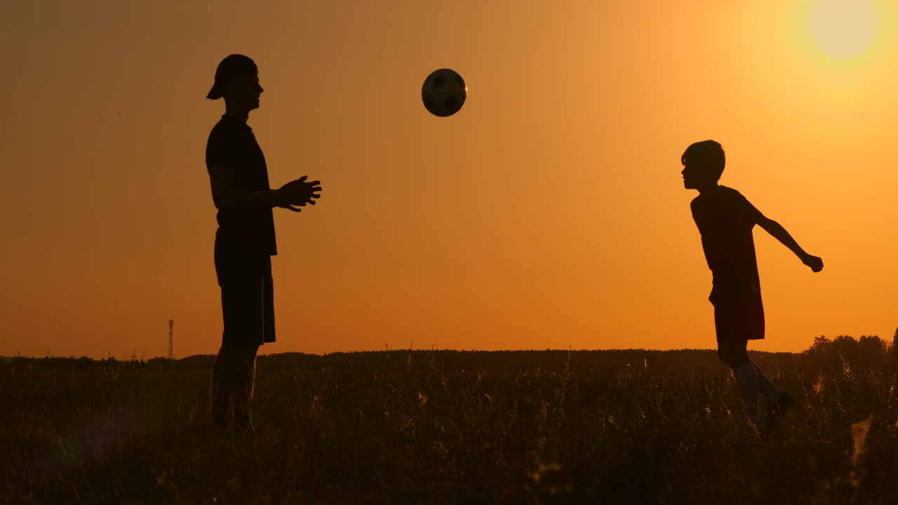 padre e hijo jugando al fútbol en el parque al atardecer siluetas contra el telón de fondo de un sol brillante disparo a cámara lenta.