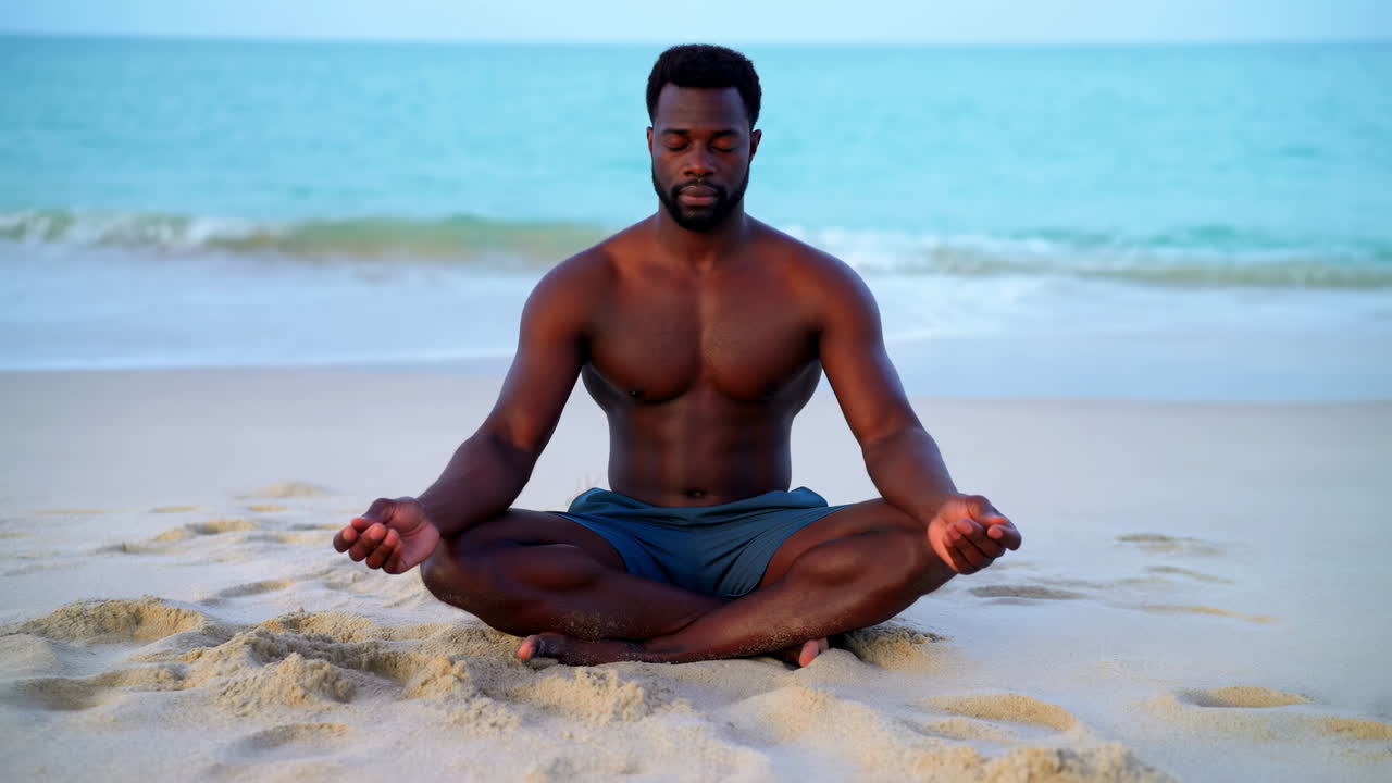 Sakin bir okyanus kenarı plajında lotus pozisyonunda meditasyon yapan adam.