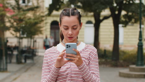 mujer joven usando teléfono inteligente escribiendo mensajes de texto navegando por internet terminando el trabajo mirando a la cámara