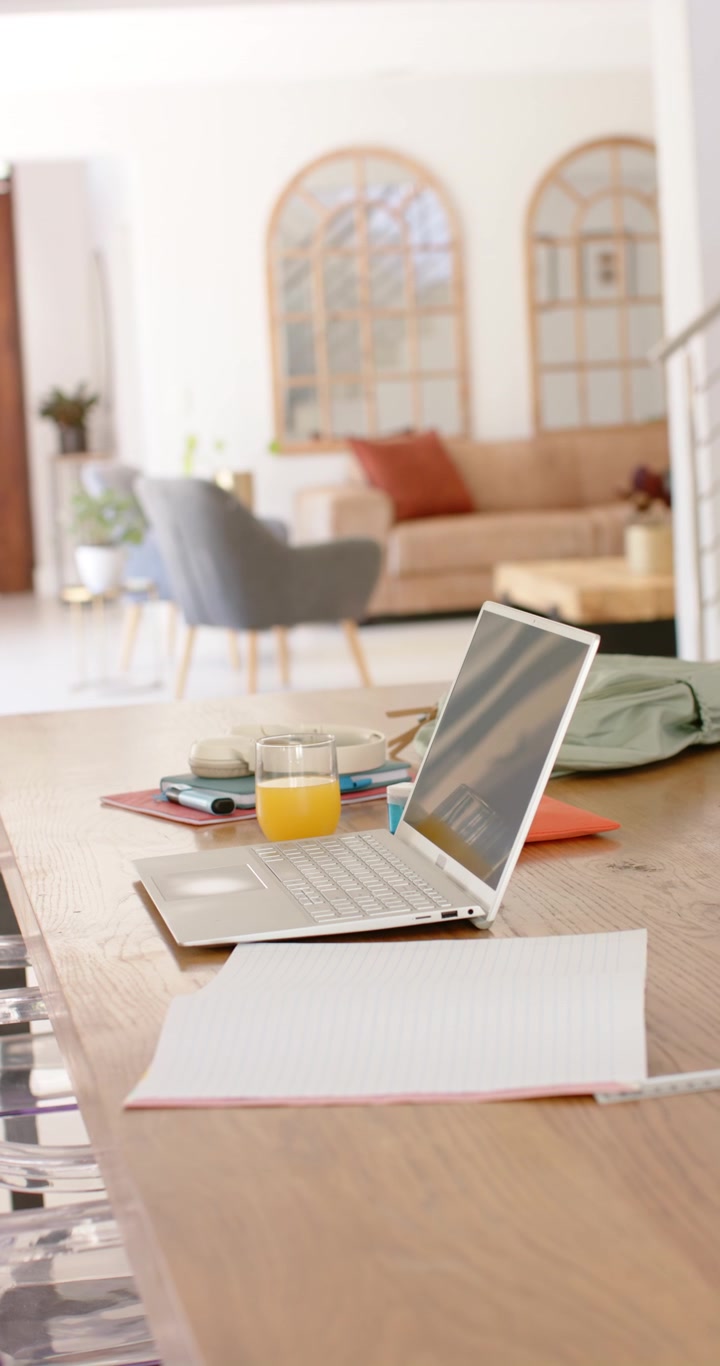 Vertical video: Camera panning inward, bringing silver laptop and glass of orange juice into focus