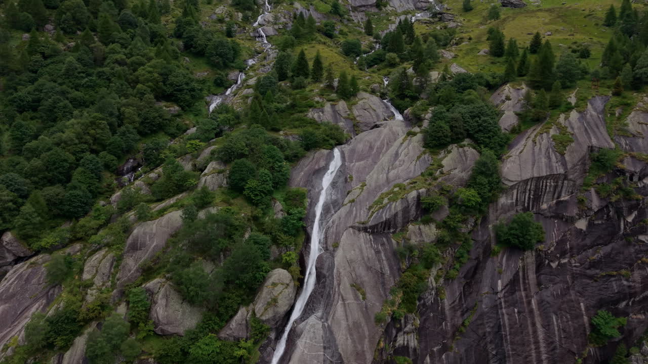 Aerial shot advancing then panning right around long waterfall on mountain ridge