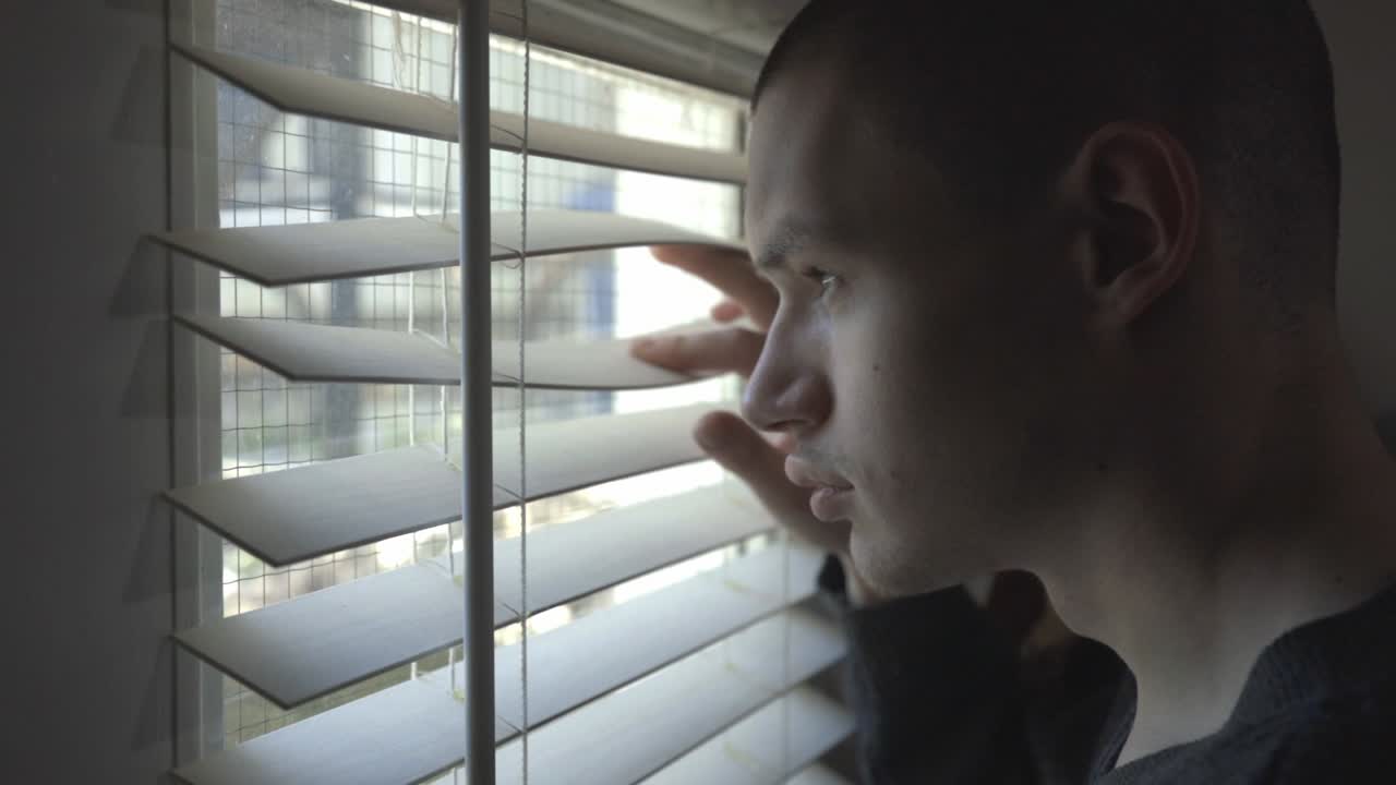Young Man Looking Outside Through The Window Blinds. - close up shot