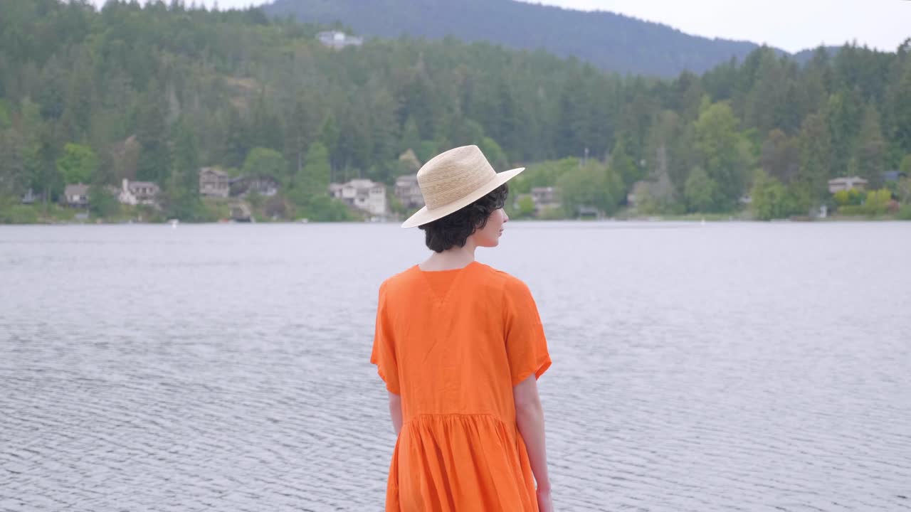 활기찬 오렌지색 드레스를 입은 여성이 호수 밖으로 걸어나가고, 후면 샷
