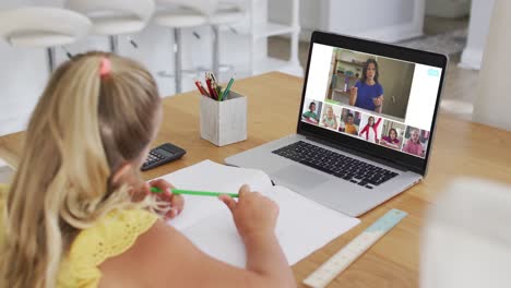 Schoolgirl-using-laptop-for-online-lesson-at-home,-with-diverse-teacher-and-class-on-screen