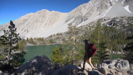 Female-Hiker-With-Backpack-in-Mountain-Landscape,-Walking-Above-Glacial-Lake-on-Sunny-Summer-Day