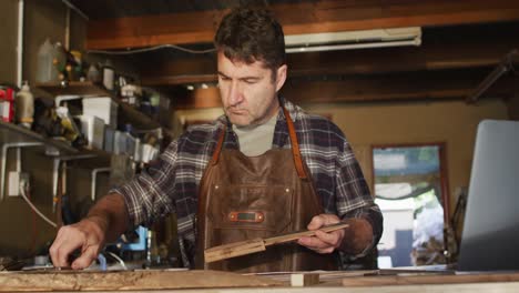 focused caucasian male knife maker in workshop holding tool and making notes