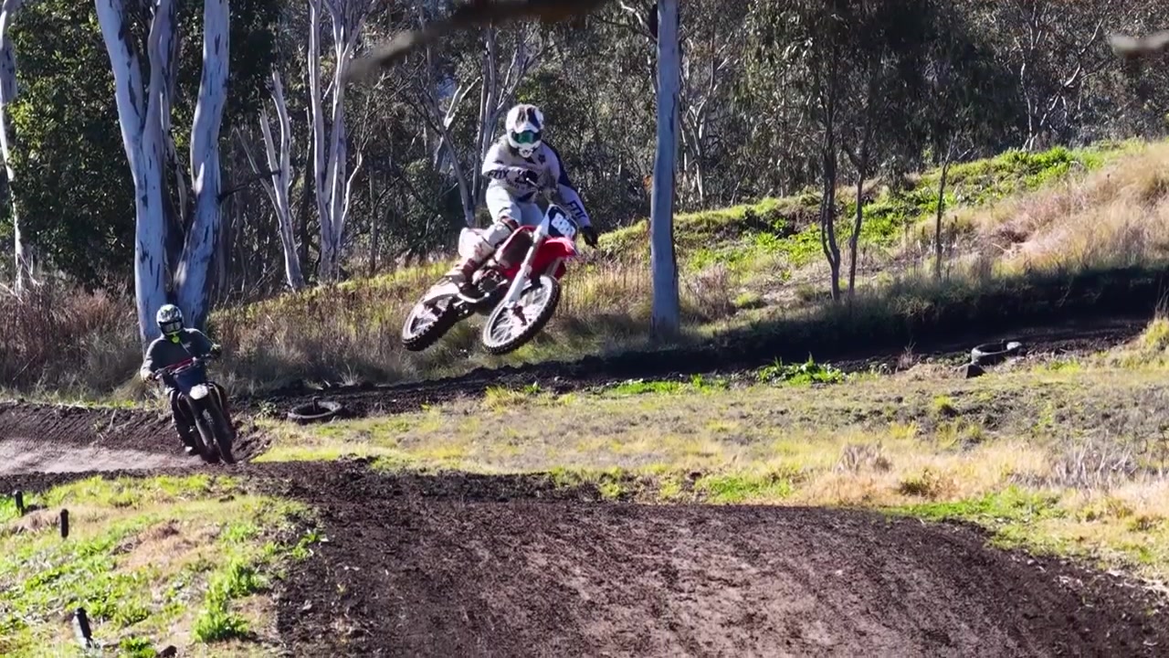 Sequência de ação de pilotos de motocross saltando e correndo em uma pista de terra emoldurada por árvores.