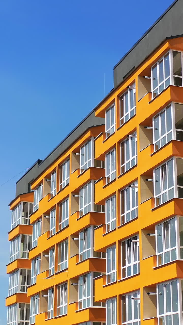 Block of flats with large balconies. Facade of a new high rise building on blue sky backdrop. Bright architecture in the city. Modern multi storey house. Vertical video