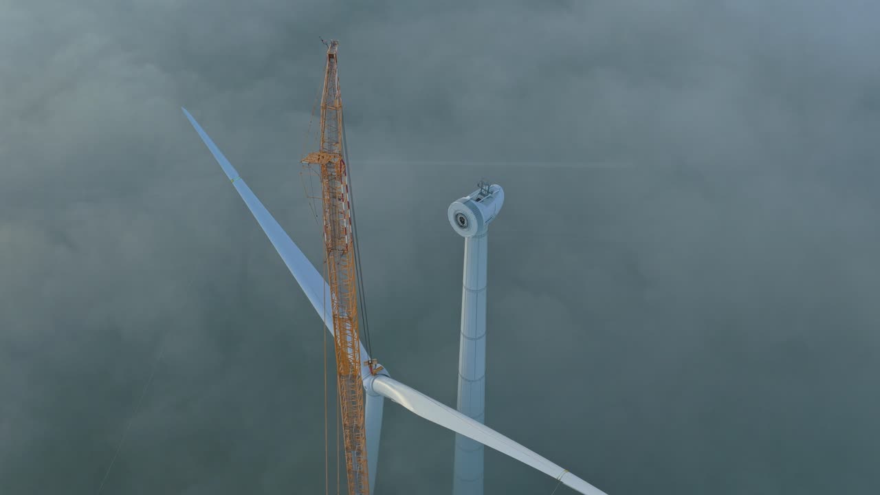 Delvist opført vindmølle i tåge med en orange kran, der monterer nye vinger.