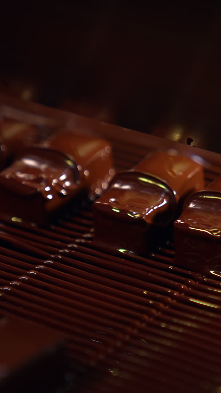Bars of sweets poured with chocolate. Chocolate bars move along conveyor belt at confectionery factory for the production of sweets. Vertical video