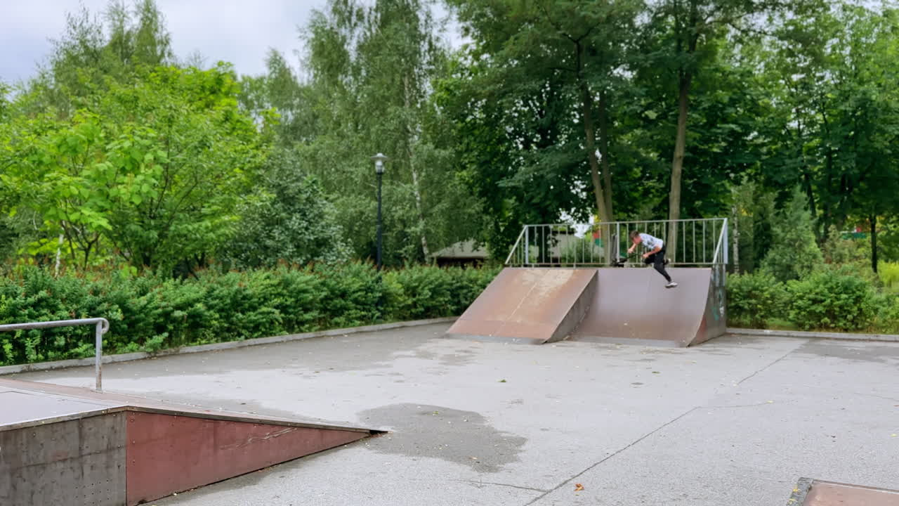 Teenage Caucasian boy riding a scooter. Young sportsman showing tricks on his scooter on the skater's ground.