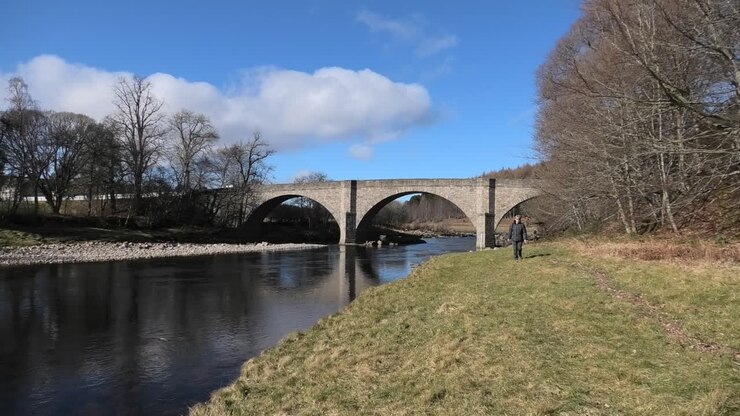 Una donna cammina verso la telecamera sul Potarch Bridge sotto il sole splendente di primavera