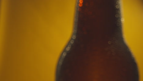 Macro-Shot-Of-Condensation-Droplets-On-Revolving-Bottle-Of-Cold-Beer-Or-Soft-Drinks-Against-Yellow-Background