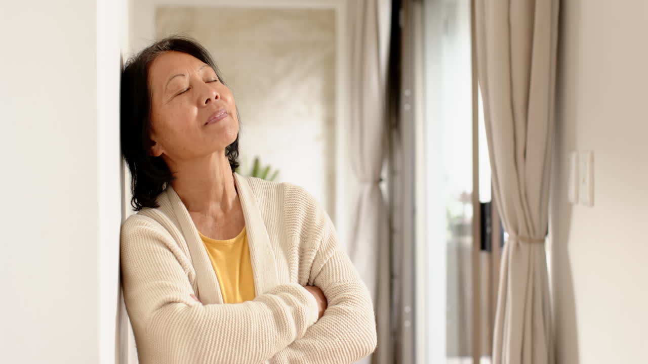 Senior Asian woman relaxing at home, smiling peacefully with eyes closed, copy space