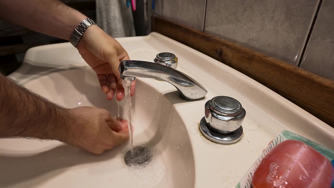 Close-up shot of a man washing hands at a bathroom sink in Argentina, using water and red soap. Warm indoor lighting, intimate composition, and focus on hygiene and cleanliness routines.