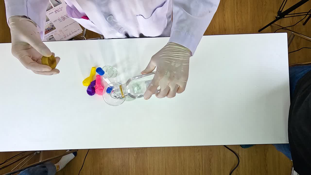 Hands in gloves perform a science experiment inflating balloons using sodium bicarbonate and vinegar on a white table