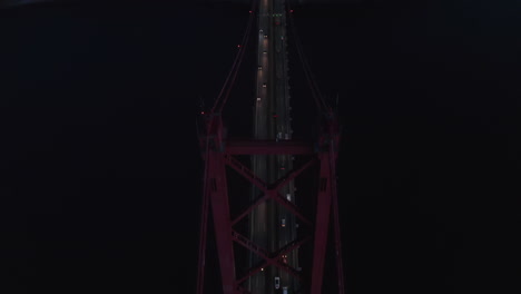 Front-aerial-into-overhead-view-of-cars-crossing-a-red-metal-Ponte-25-de-Abril-hanging-bridge-over-sea-near-Lisbon,-Portugal